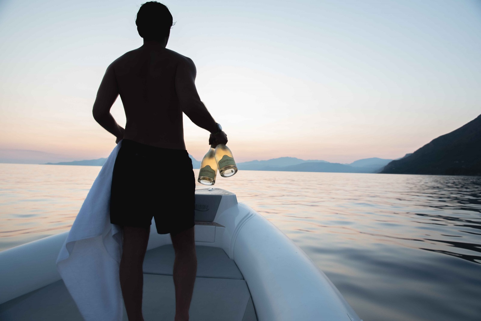 Silhouette di un uomo a prua con due bottiglie di prosecco al crepuscolo